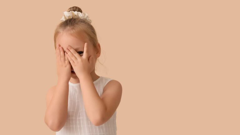 A young child hiding their face with their hands, representing a gentle moment connected to autism and eye contact