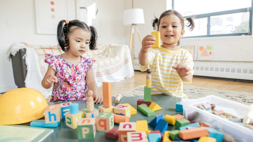 Autism and playdates scene with two kids building with letter blocks and shapes in a tidy, light‑filled space