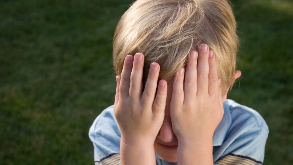Child covering their face with their hands to show how eye contact can feel overwhelming for some children on the spectrum