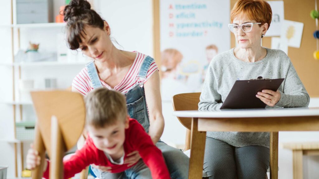 Child moving energetically as two adults observe and record details in a setting that suggests an assessment for ADHD and autism