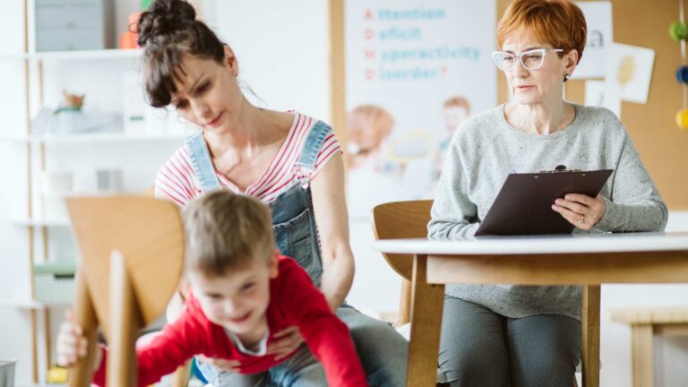 Child moving energetically as two adults observe and record details in a setting that suggests an assessment for ADHD and autism