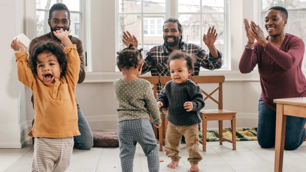 Parents cheer while toddlers play together on the floor, showing warm support during an autism‑friendly playdate