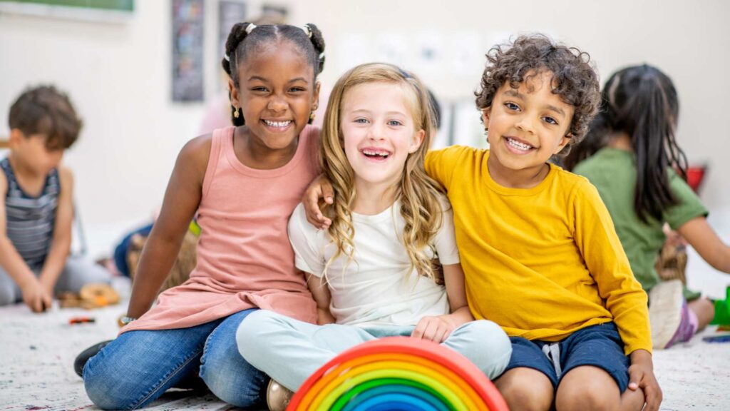 Three smiling kids sitting close together in a classroom, showing warm friendship and inclusion for autistic children