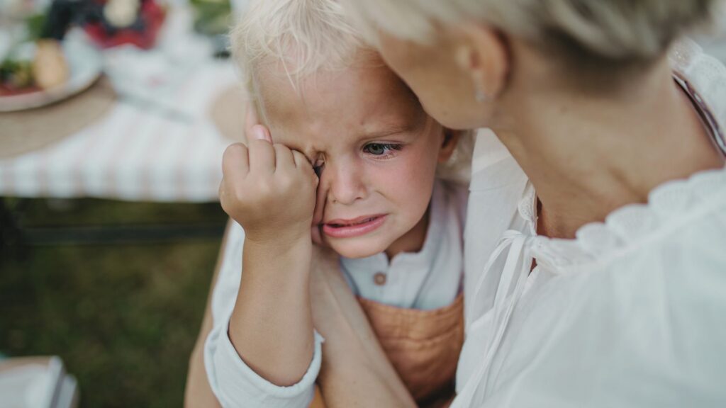 Toddler having a tantrum while being comforted by a parent outdoors, showing signs of distress and emotional overwhelm.