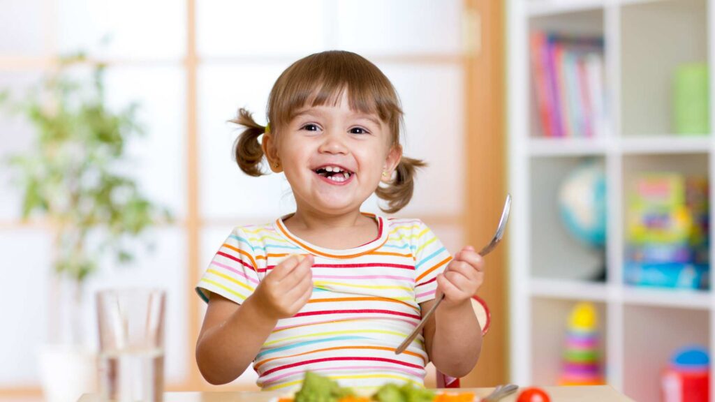 Toddler smiling during a mealtime daily routine, independent skill supported by ABA therapy for toddlers