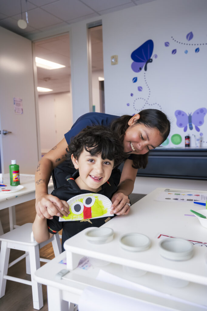 Child and therapist smiling during ABA therapy craft activity